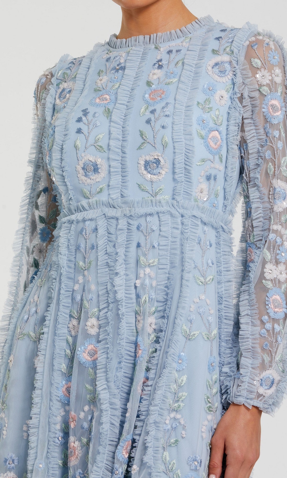 A person wearing the Mac Duggal 9365 short wedding guest dress, featuring light blue floral embroidery, sheer long sleeves, and ruffle details.